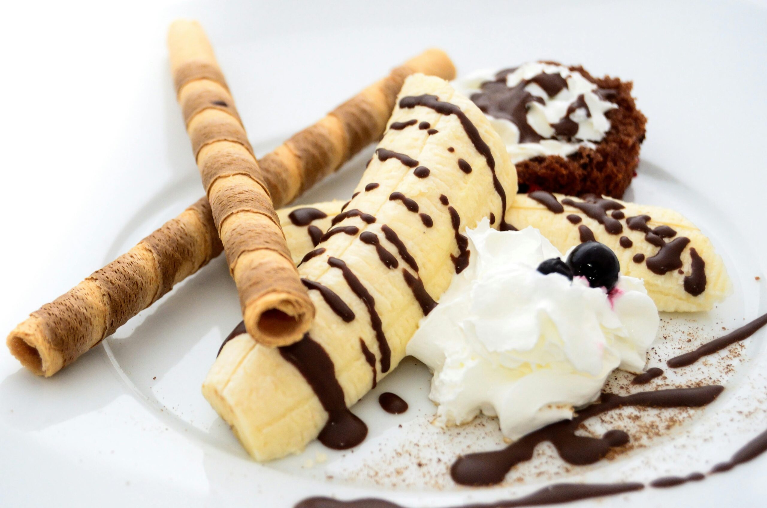 Close-up of a banana dessert with chocolate drizzle, whipped cream, and wafer sticks.